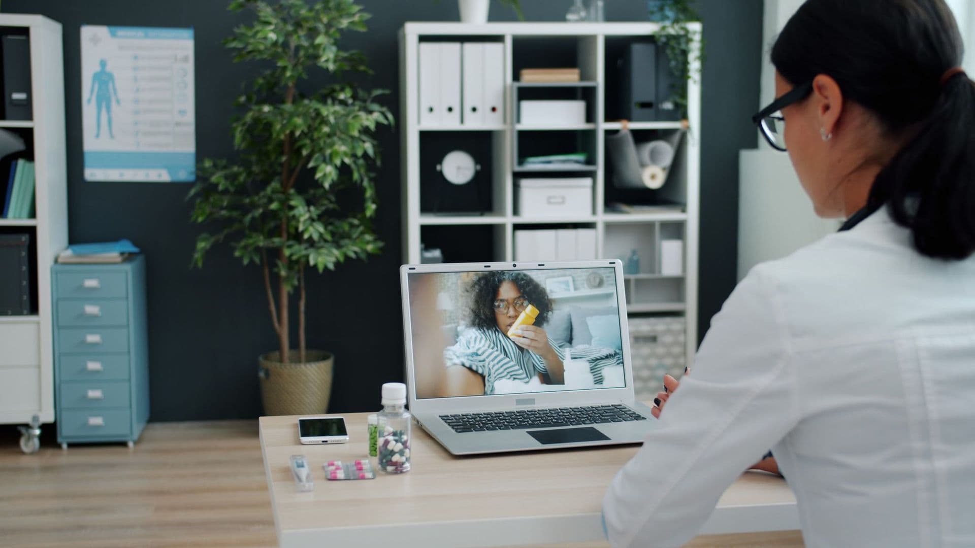 A pharmacist holds a video consultation with a patient on a laptop.