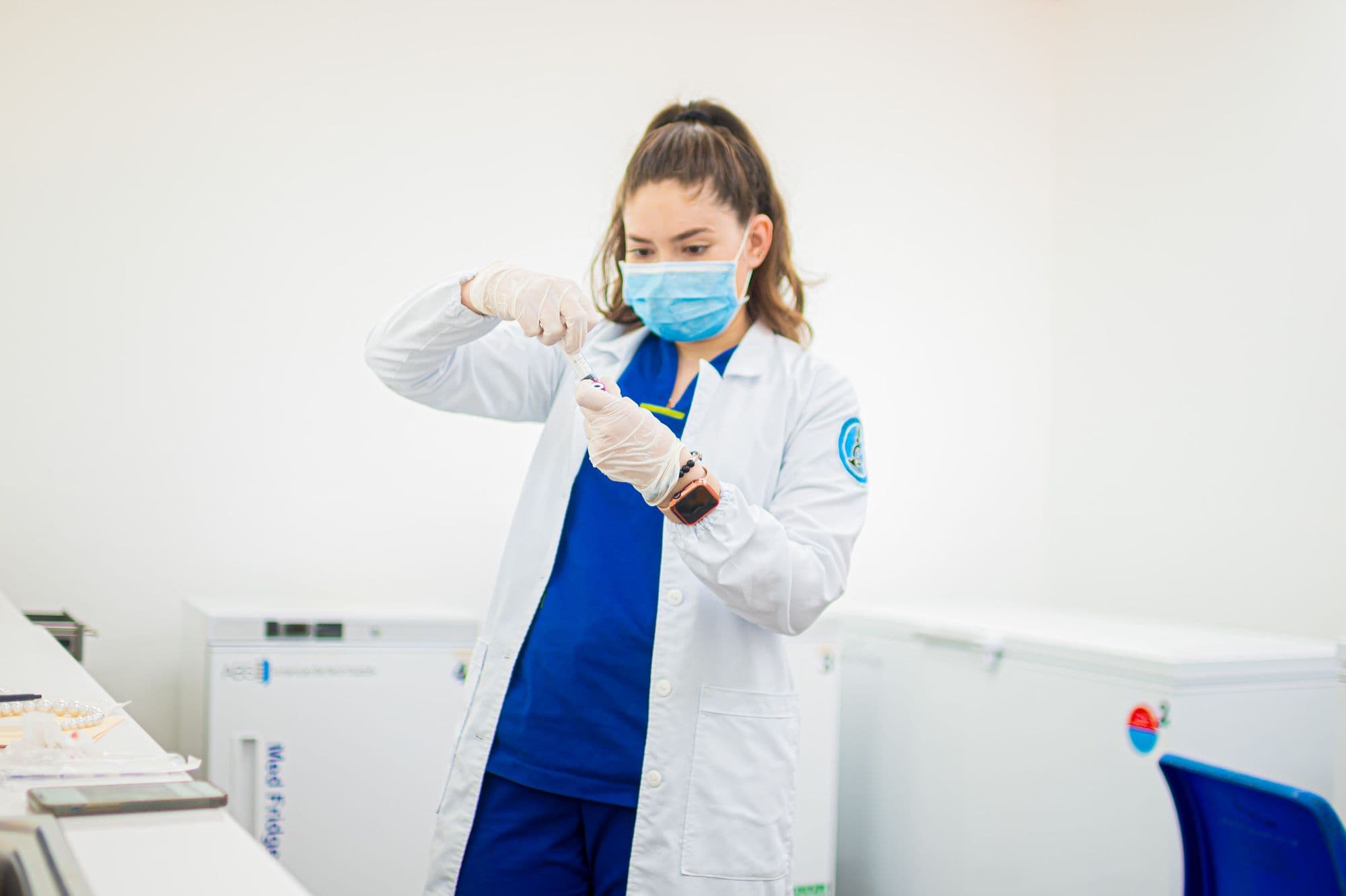 A pharmacy technician in a mask and gloves prepares a medication in a clean workspace.