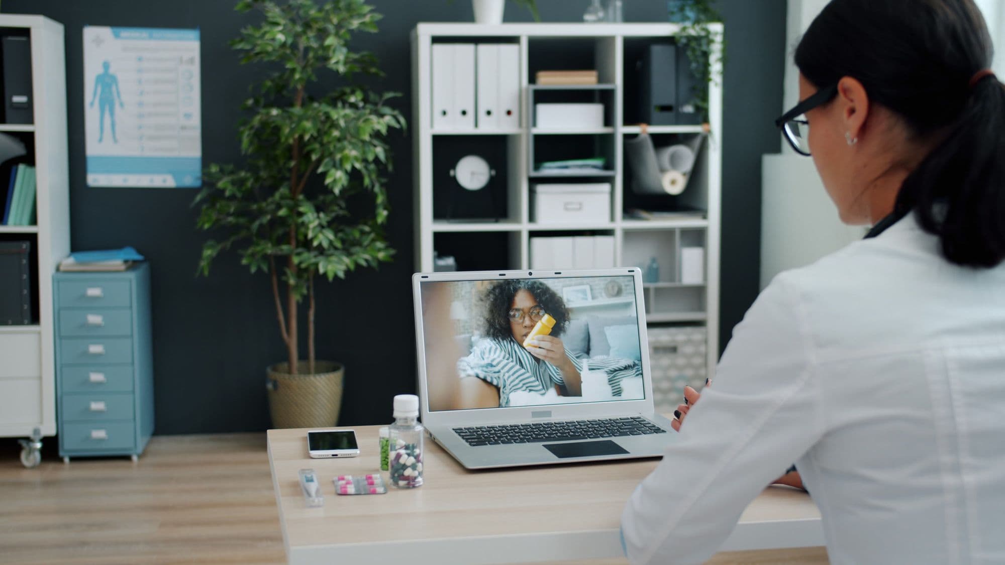 A pharmacist holds a video consultation with a patient on a laptop.