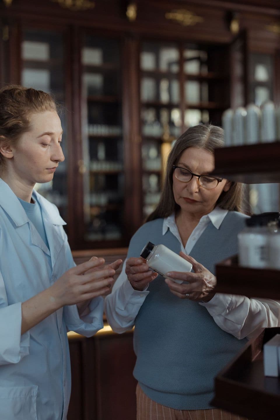 A pharmacist shows a medication package to an older woman at a pharmacy counter.